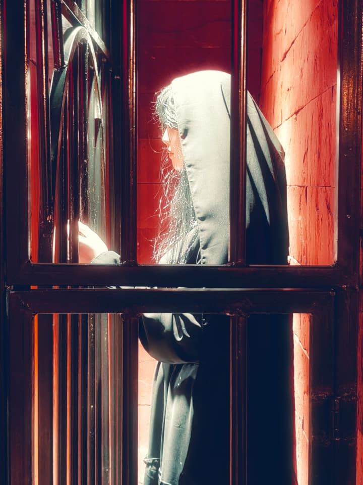 A hooded figure behind the bars of a cell